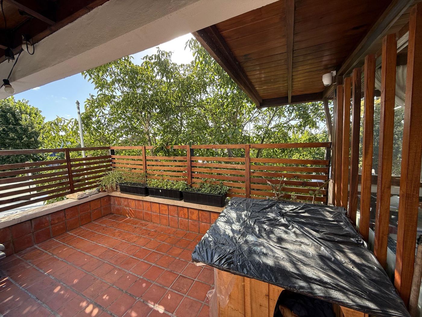 Balcón terraza con piso de baldosa roja, pérgola de madera y vista a los árboles
